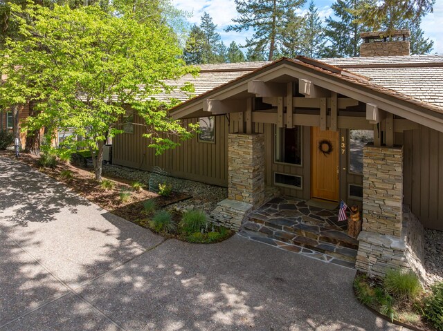 view of exterior entry with board and batten siding, stone siding, and a chimney