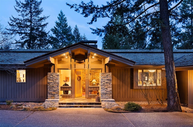 view of exterior entry featuring board and batten siding, stone siding, and a shingled roof