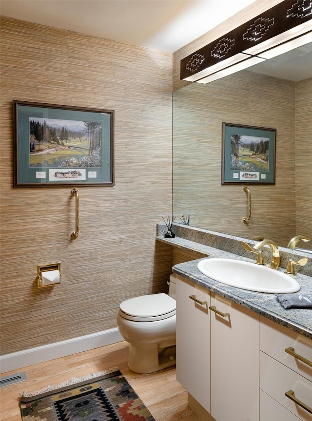 half bath with vanity, toilet, wood finished floors, and visible vents