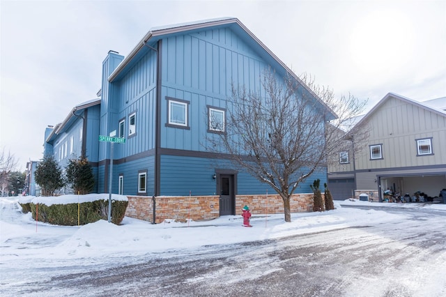 119 Oak St, Whitefish, MT 59937 - view of snow covered exterior with board and batten siding, an attached garage, stone siding, and a chimney