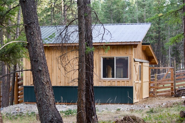 view of side of property featuring metal roof, a wooded view, and fence