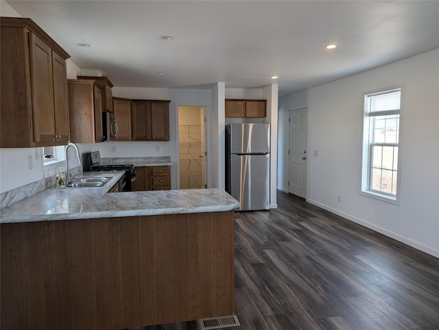 kitchen featuring dark wood-type flooring, baseboards, appliances with stainless steel finishes, a peninsula, and a sink