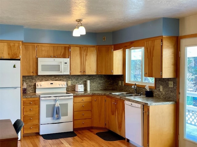 kitchen featuring light wood finished floors, tasteful backsplash, brown cabinetry, white appliances, and a sink