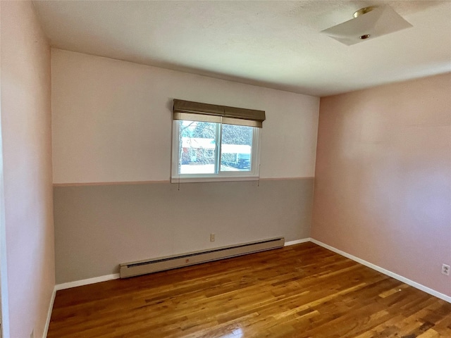 unfurnished room with a baseboard heating unit, wood finished floors, and baseboards