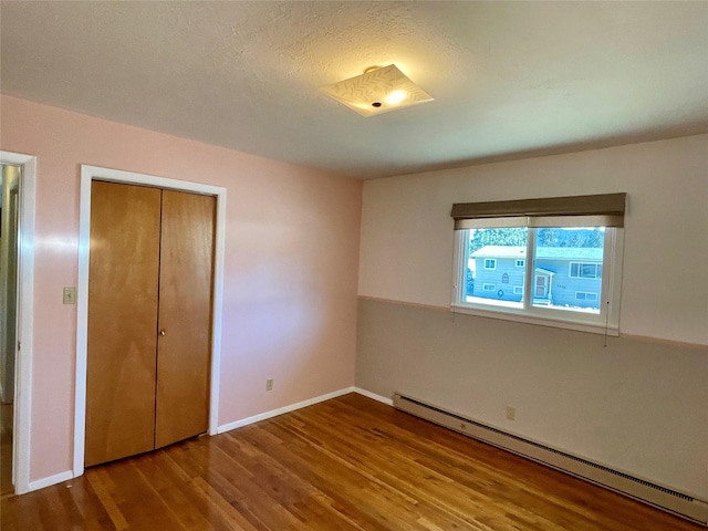 unfurnished bedroom with a baseboard heating unit, baseboards, a closet, and wood finished floors