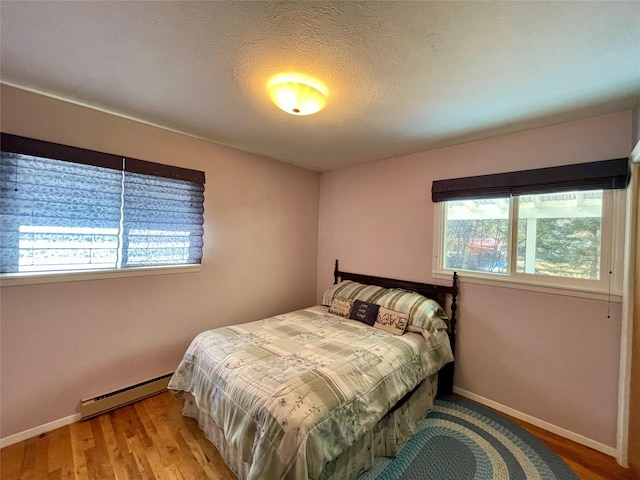 bedroom with a textured ceiling, baseboards, a baseboard heating unit, and light wood-style floors