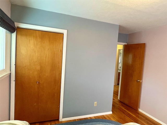 unfurnished bedroom featuring wood finished floors, baseboards, and a closet