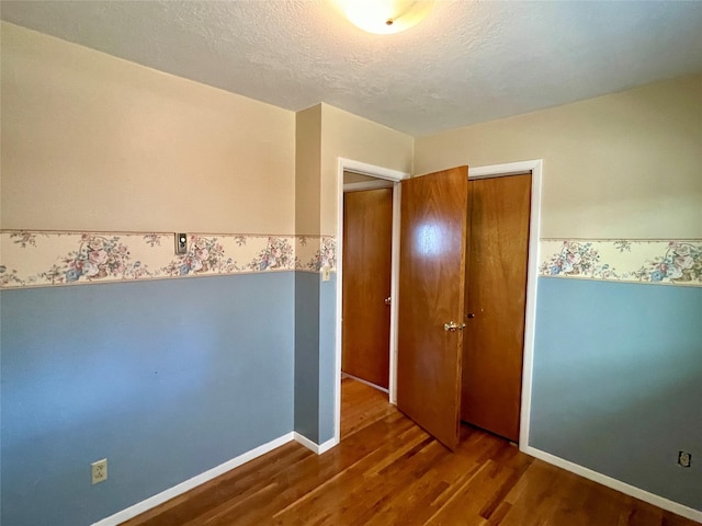 unfurnished bedroom with baseboards, wood finished floors, a closet, and a textured ceiling