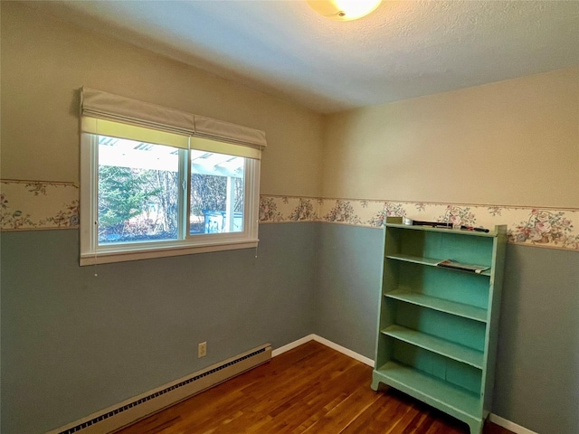 empty room featuring wallpapered walls, baseboards, dark wood finished floors, baseboard heating, and wainscoting