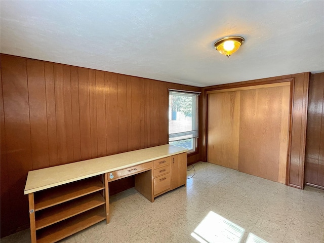 unfurnished office with wooden walls, light floors, and built in study area