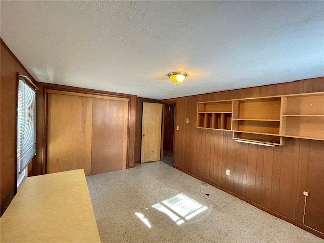 unfurnished bedroom with tile patterned floors, wooden walls, a textured ceiling, and a closet