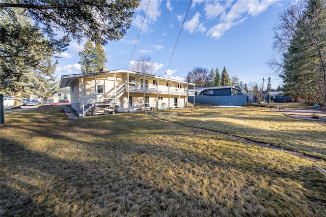 rear view of property featuring a lawn, stairs, and fence