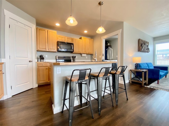 kitchen featuring dark wood-type flooring, light brown cabinets, a breakfast bar area, light countertops, and range