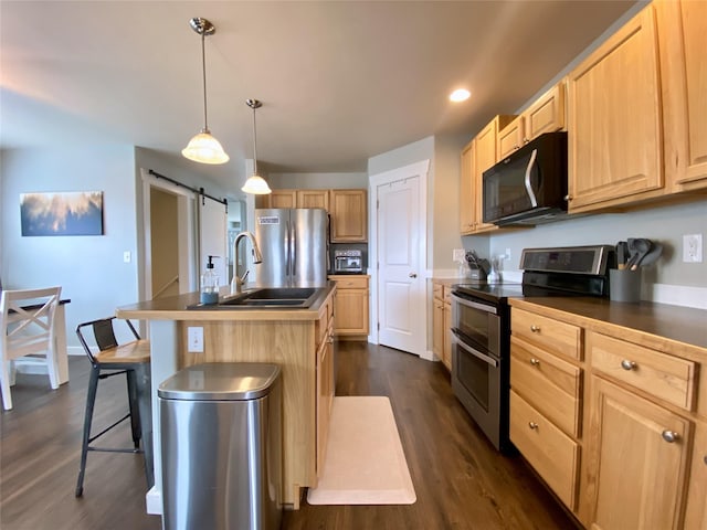 kitchen featuring dark countertops, light brown cabinets, dark wood finished floors, a barn door, and stainless steel appliances