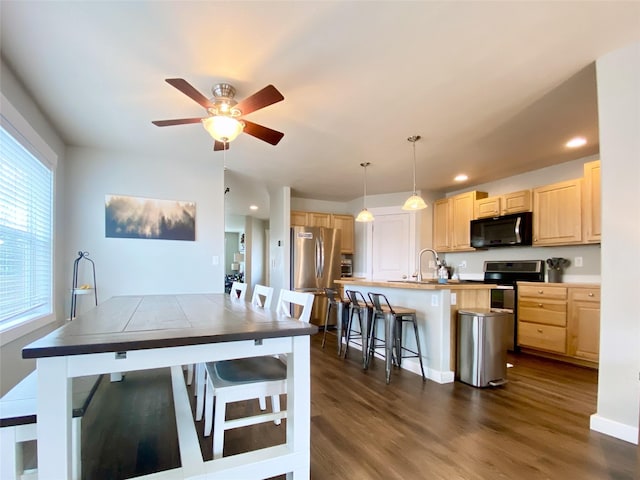 kitchen featuring a center island with sink, light brown cabinets, dark wood-style floors, stainless steel appliances, and a breakfast bar area