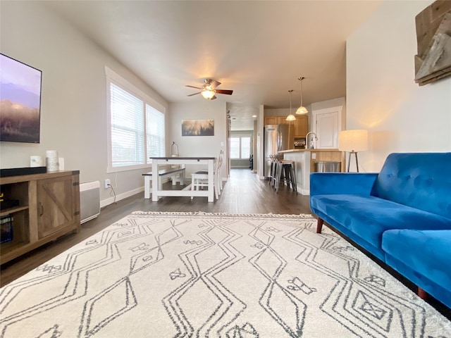 living area with baseboards, dark wood-type flooring, and a ceiling fan