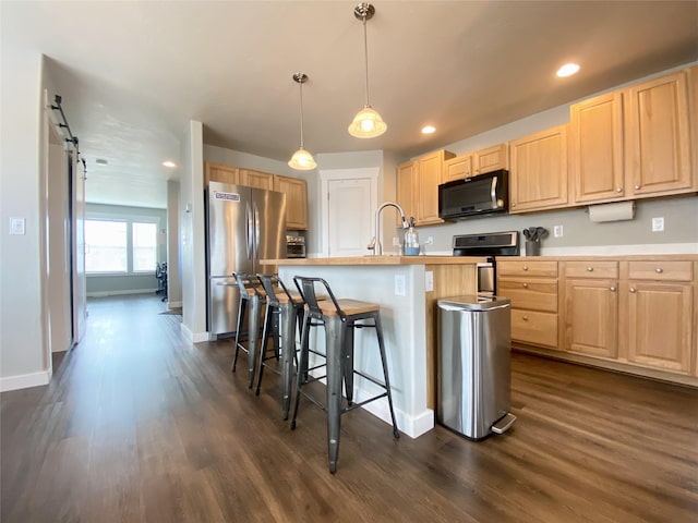 kitchen with a breakfast bar, light brown cabinets, a barn door, appliances with stainless steel finishes, and dark wood-style flooring