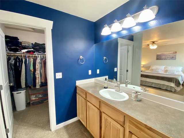 bathroom with vanity, a spacious closet, a ceiling fan, and baseboards