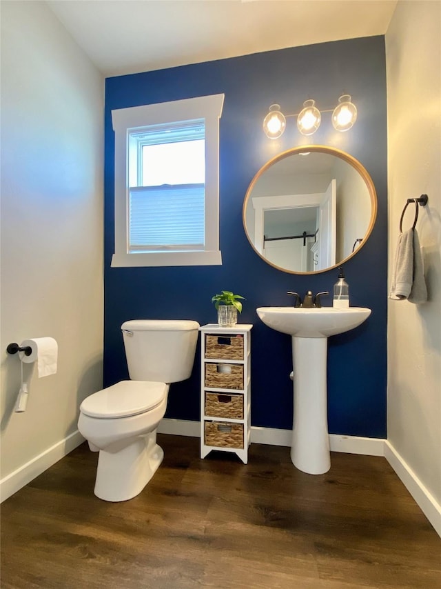 half bathroom with a sink, baseboards, toilet, and wood finished floors