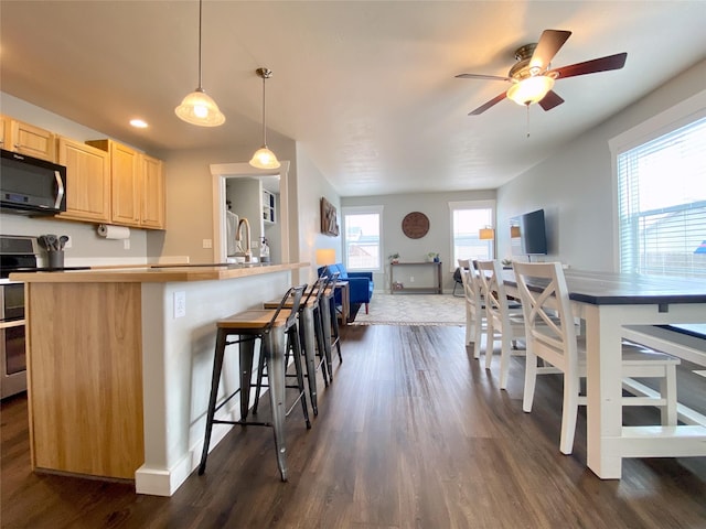 kitchen with light brown cabinets, baseboards, dark wood finished floors, a kitchen breakfast bar, and electric range