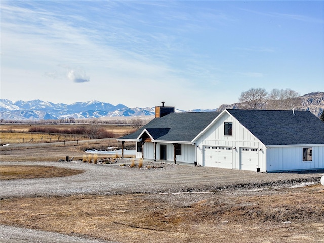 view of front of home with a shingled roof, a chimney, dirt driveway, board and batten siding, and a mountain view