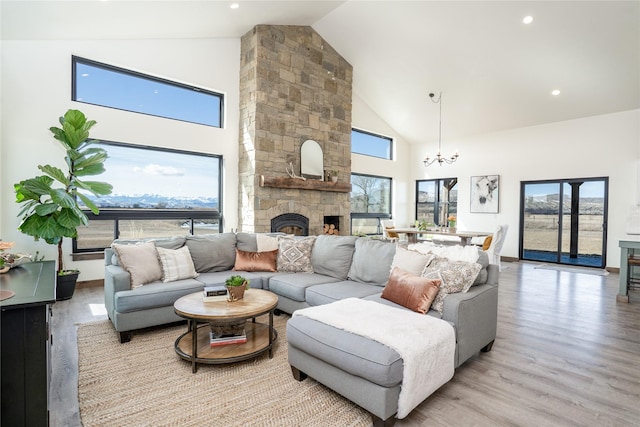 living area with light wood-type flooring, high vaulted ceiling, a stone fireplace, baseboards, and a chandelier