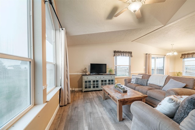 living area with baseboards, lofted ceiling, hardwood / wood-style flooring, a textured ceiling, and ceiling fan with notable chandelier