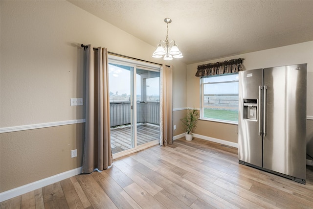 unfurnished dining area featuring a notable chandelier, a textured ceiling, baseboards, light wood-style floors, and lofted ceiling