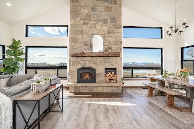 living area with a stone fireplace, high vaulted ceiling, an inviting chandelier, and wood finished floors