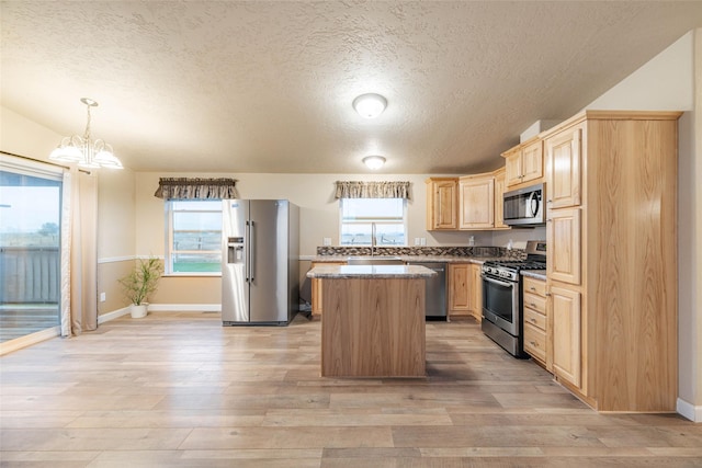 kitchen with light brown cabinetry, a kitchen island, light wood-style floors, appliances with stainless steel finishes, and an inviting chandelier