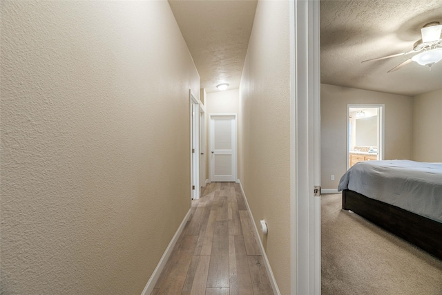 corridor with a textured ceiling, light wood-style floors, baseboards, and a textured wall