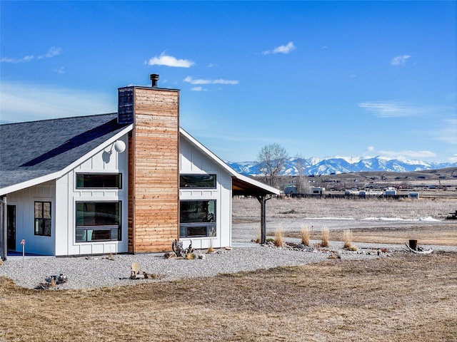 view of side of property featuring a mountain view, a chimney, and a shingled roof