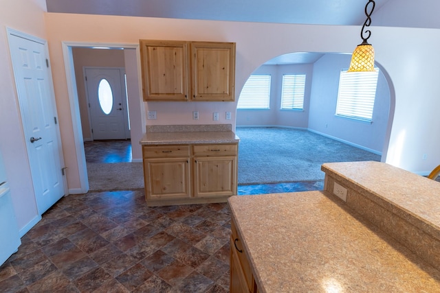 kitchen featuring arched walkways, light brown cabinetry, and dark colored carpet