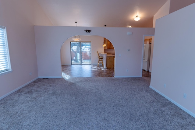 spare room featuring arched walkways, baseboards, carpet, and vaulted ceiling