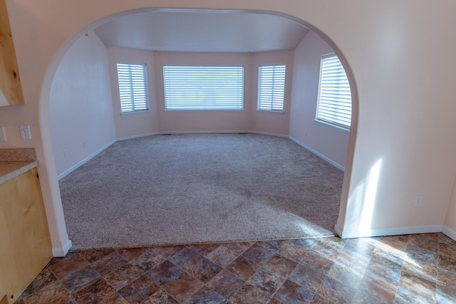 empty room featuring plenty of natural light, baseboards, dark colored carpet, and stone finish flooring