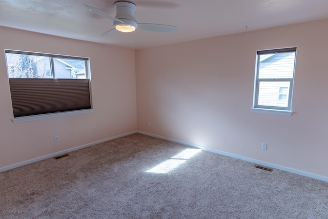 carpeted spare room featuring baseboards, visible vents, and ceiling fan