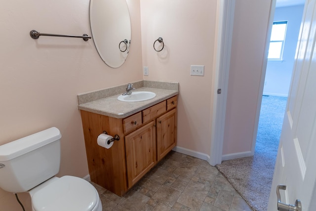 bathroom featuring baseboards, toilet, vanity, and stone finish floor