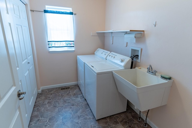 clothes washing area with washing machine and clothes dryer, baseboards, laundry area, stone finish floor, and a sink