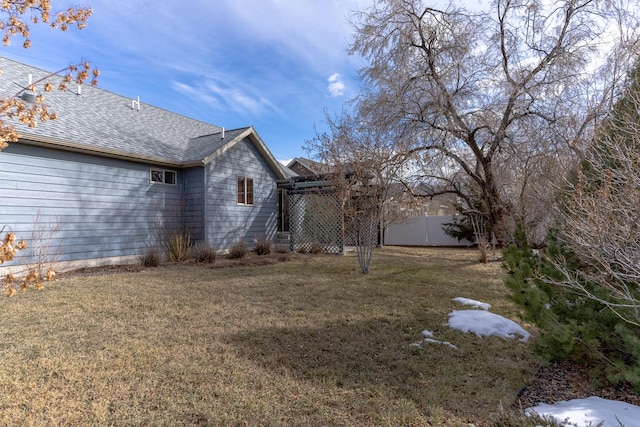 exterior space featuring a yard, fence, and a shingled roof