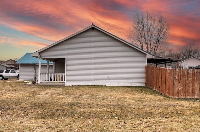 view of property exterior featuring metal roof, a lawn, a porch, and fence