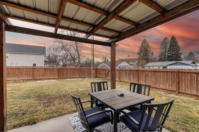 patio terrace at dusk featuring outdoor dining space, a yard, a fenced backyard, and a residential view