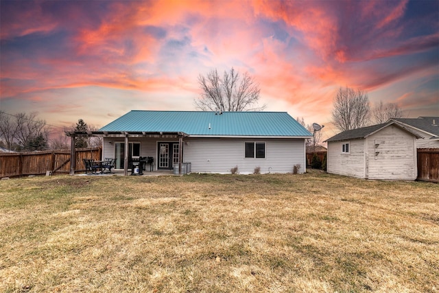 back of property at dusk with central air condition unit, metal roof, a yard, a fenced backyard, and a patio area