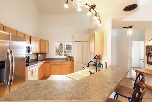 kitchen with light brown cabinetry, appliances with stainless steel finishes, a peninsula, light tile patterned flooring, and a sink