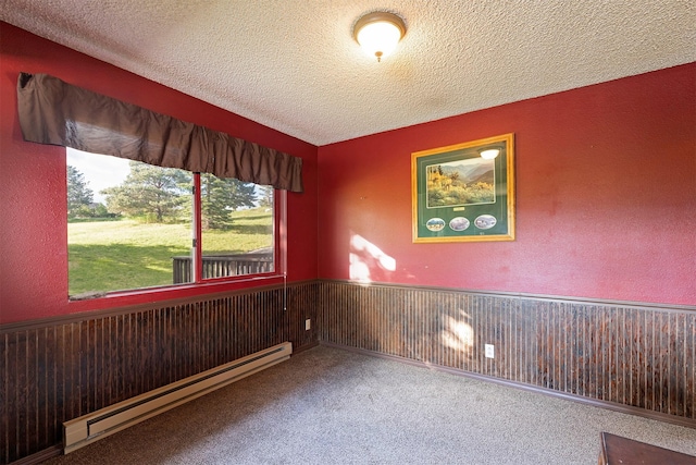 spare room featuring a baseboard heating unit, a textured ceiling, wainscoting, and carpet