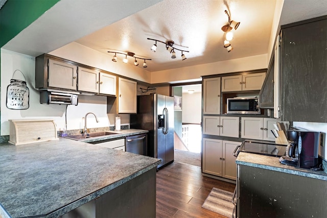 kitchen featuring dark wood-type flooring, a sink, a textured ceiling, stainless steel appliances, and a peninsula