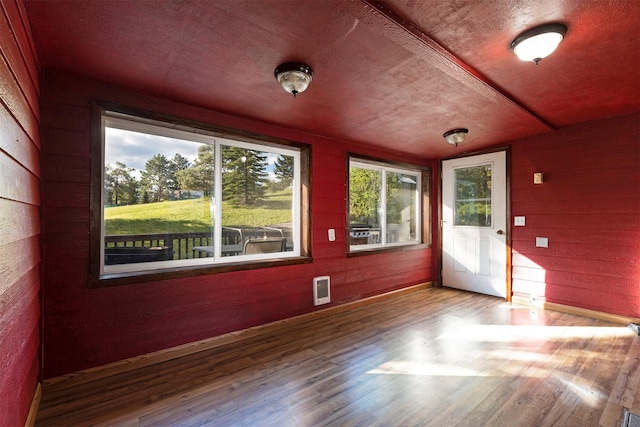 empty room featuring wood walls, a textured ceiling, and wood finished floors