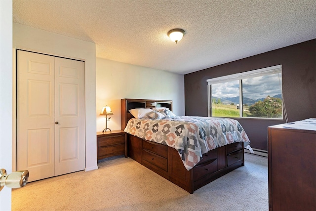 bedroom featuring light colored carpet, baseboard heating, and a textured ceiling