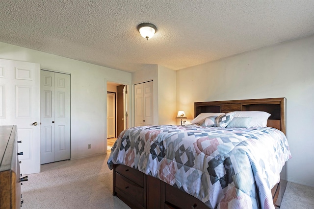 bedroom featuring light carpet, a textured ceiling, baseboards, and multiple closets