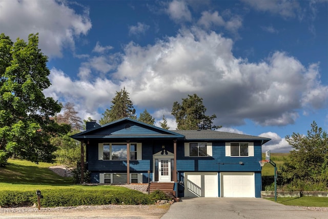 raised ranch featuring concrete driveway, an attached garage, a front yard, and a chimney