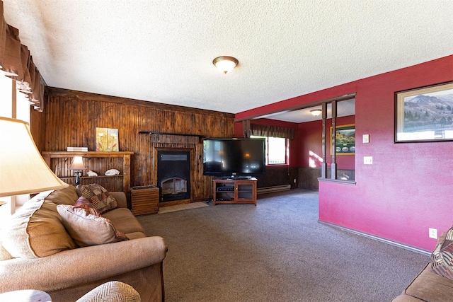 living area featuring wooden walls, carpet, a baseboard radiator, a fireplace with flush hearth, and a textured ceiling